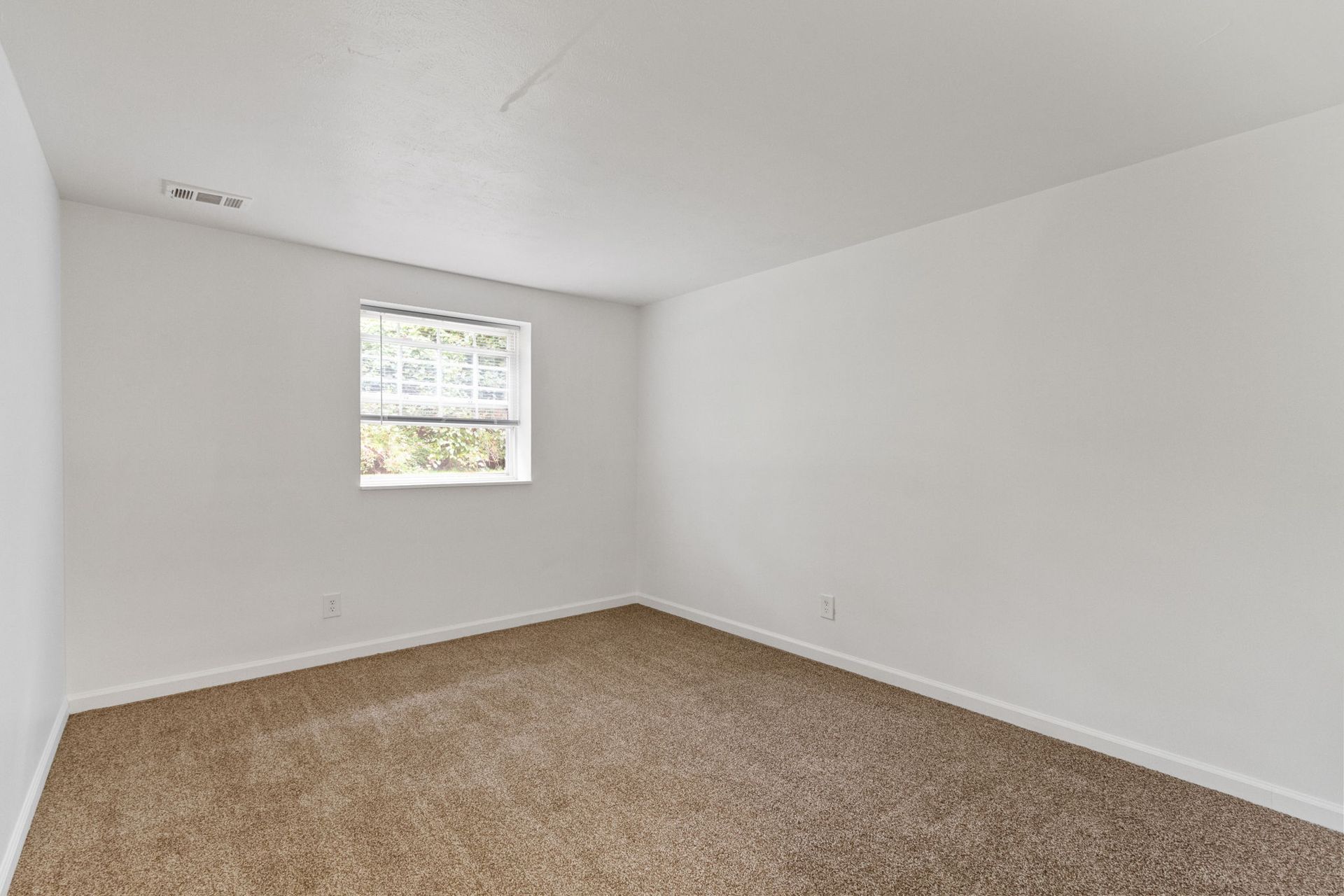 Empty room with tan carpet, white walls, and a small window.