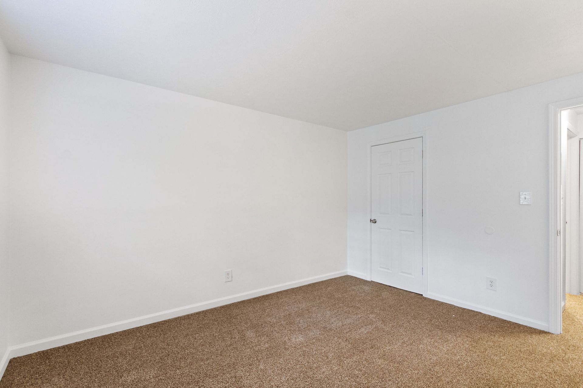 Empty room with tan carpet, white walls, and a closed white door.