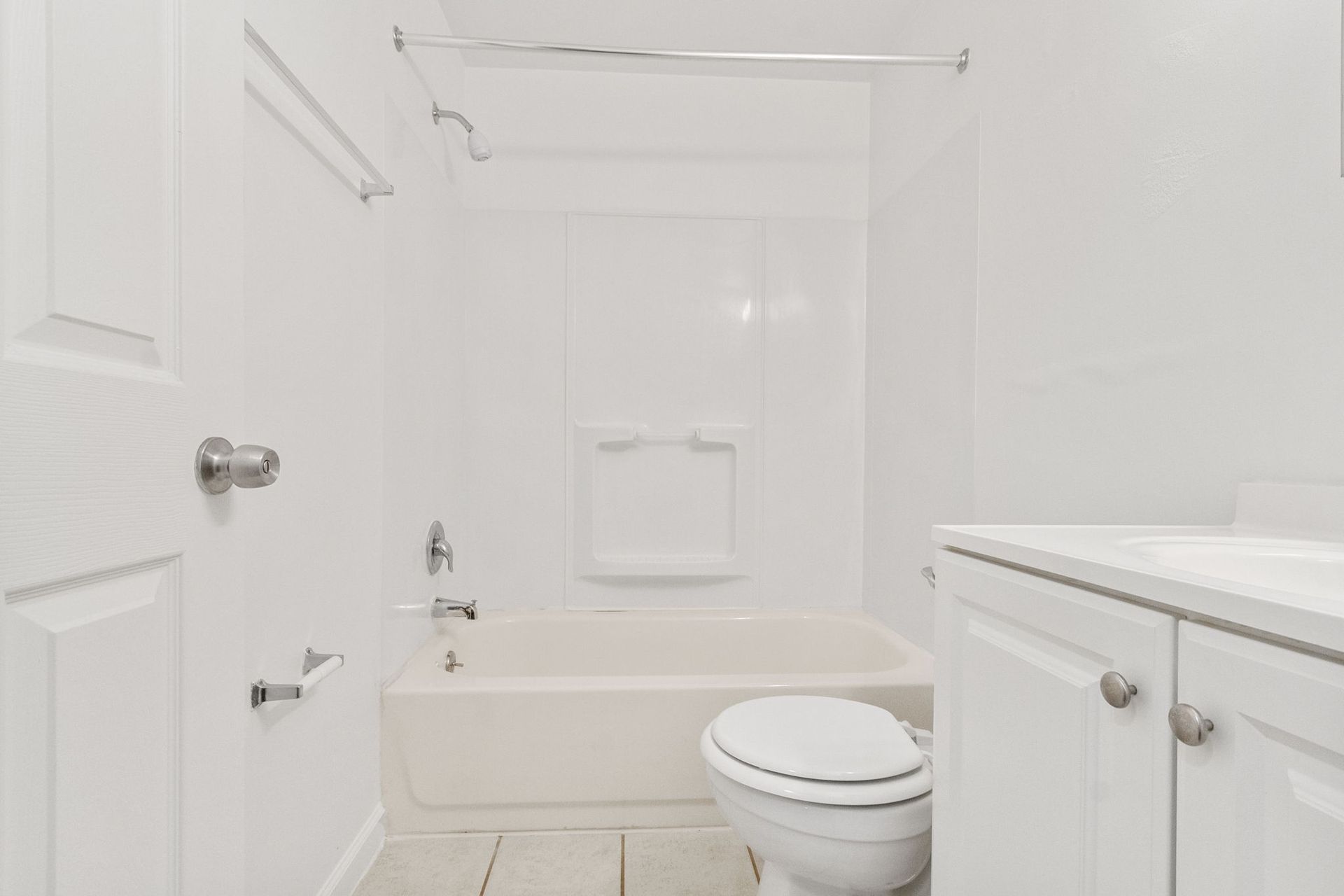 White bathroom with a tub, toilet, vanity, and a closed door.