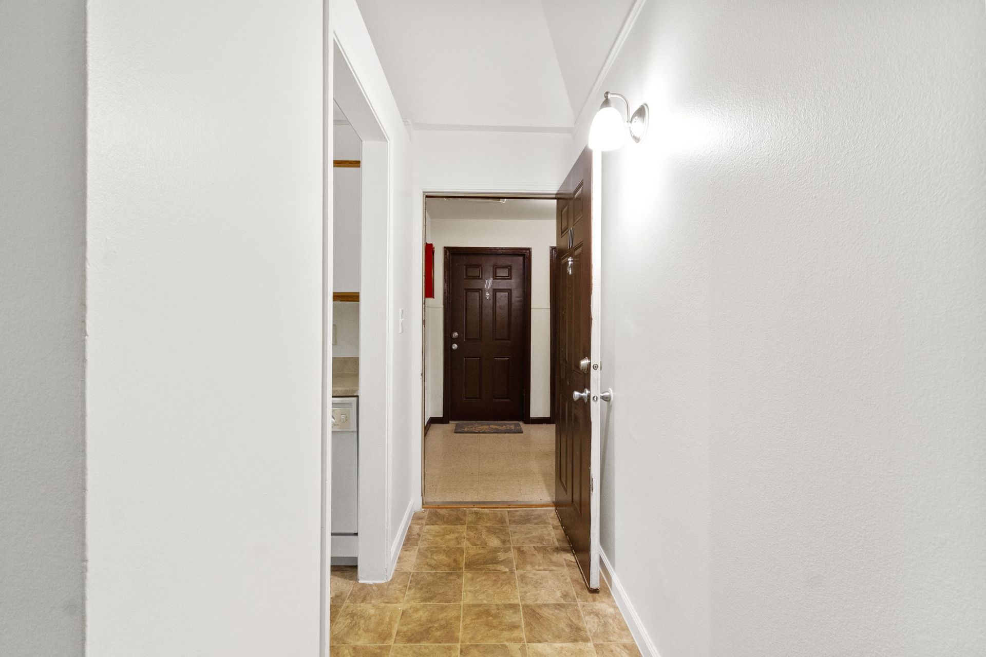 Narrow hallway with brown door at the end and white walls.