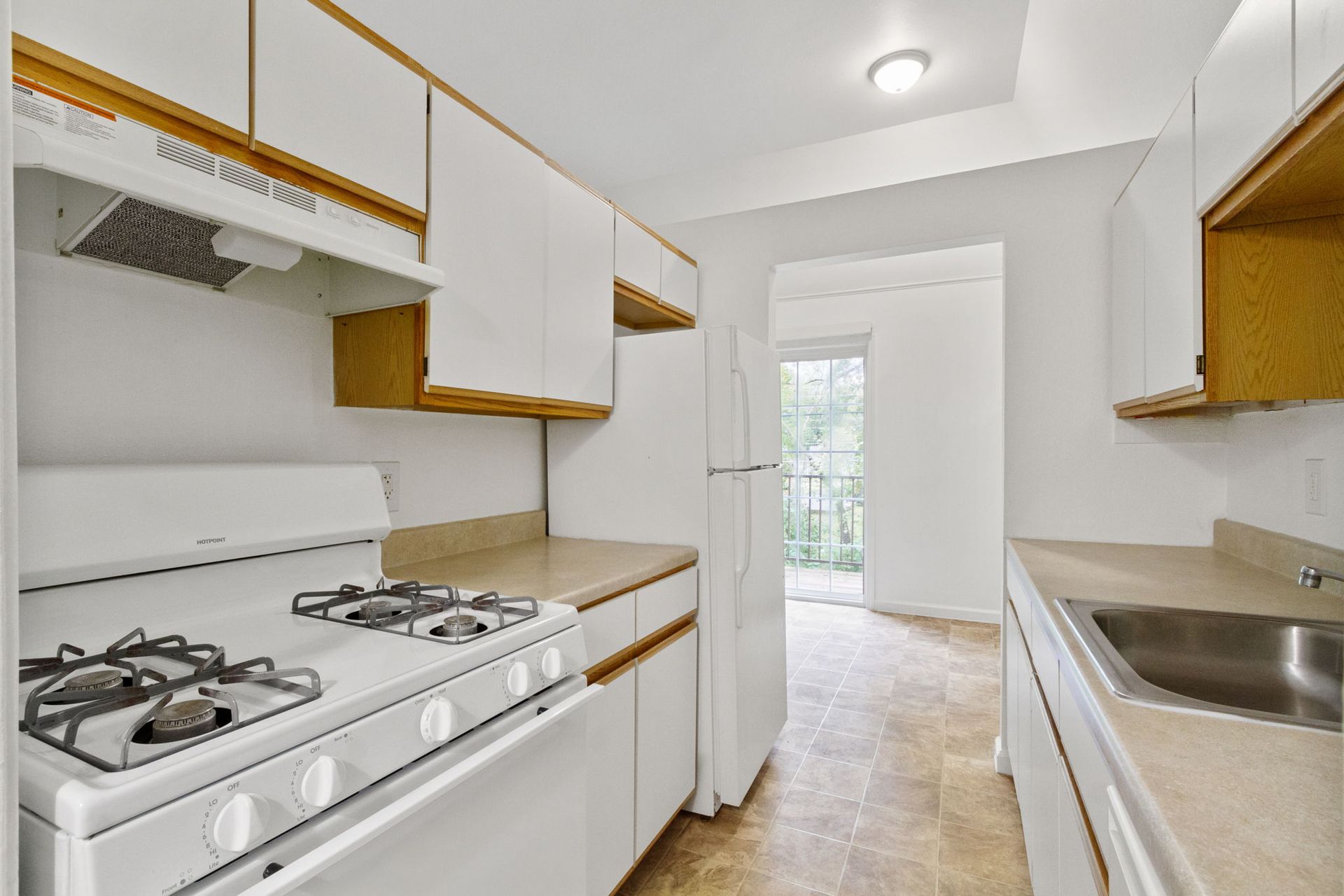 White kitchen with gas stove, cabinets, refrigerator, and a door leading to a balcony.