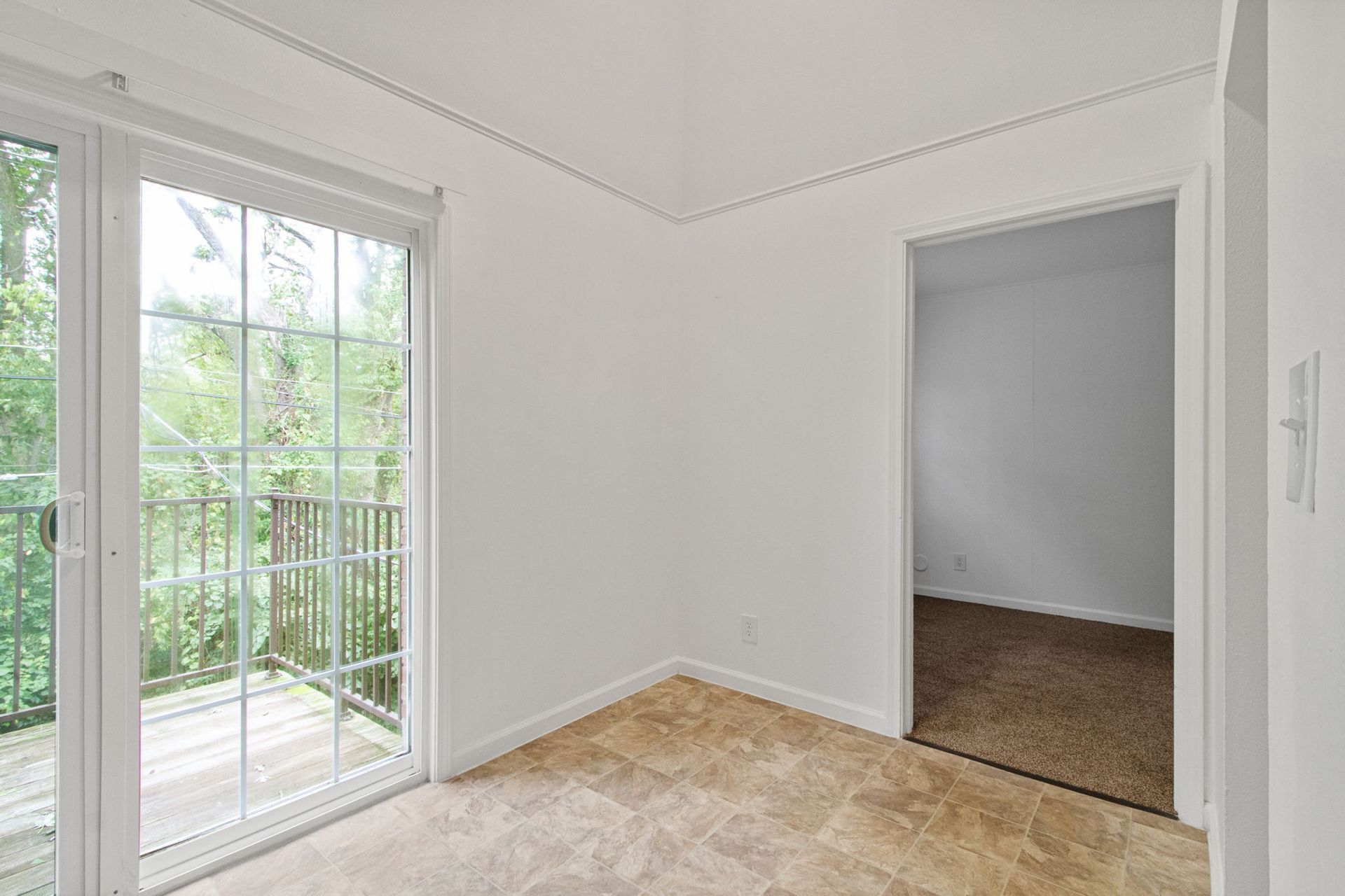 Empty room with sliding glass door to a balcony, and a doorway leading to another room. Beige carpet.