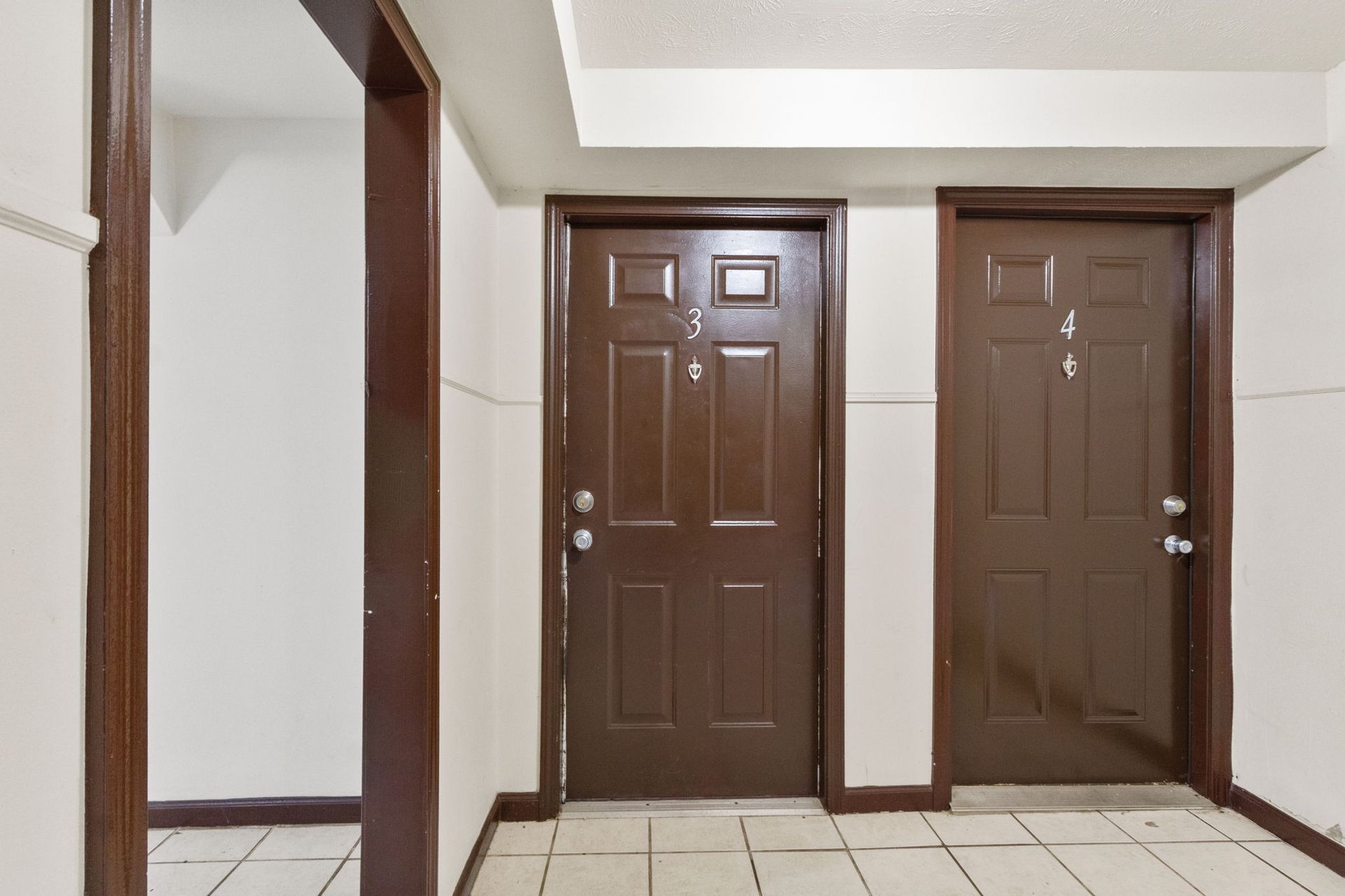 Hallway with two brown doors, white walls, and tiled floor.