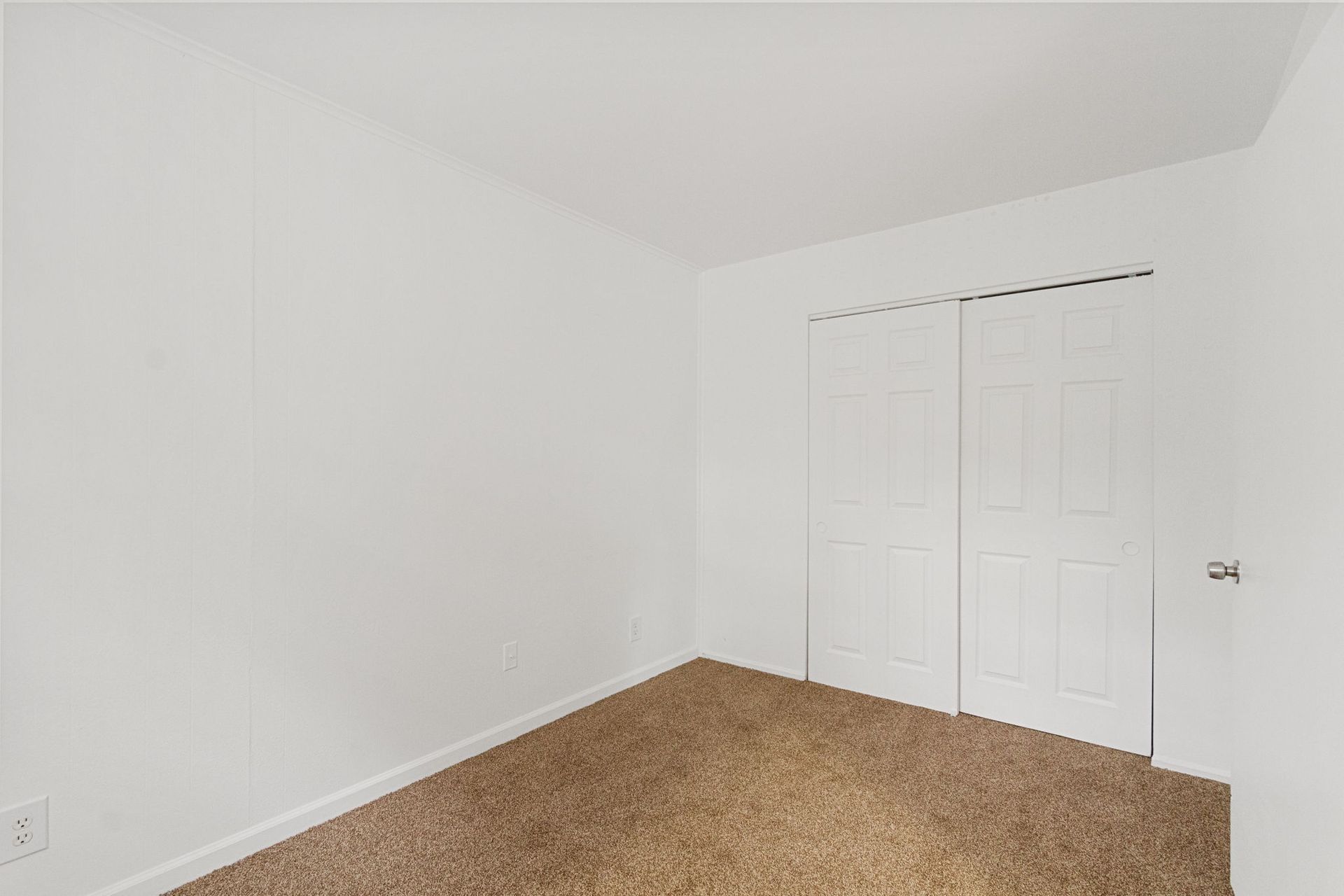Empty bedroom with beige carpet, white walls, and a closed closet.