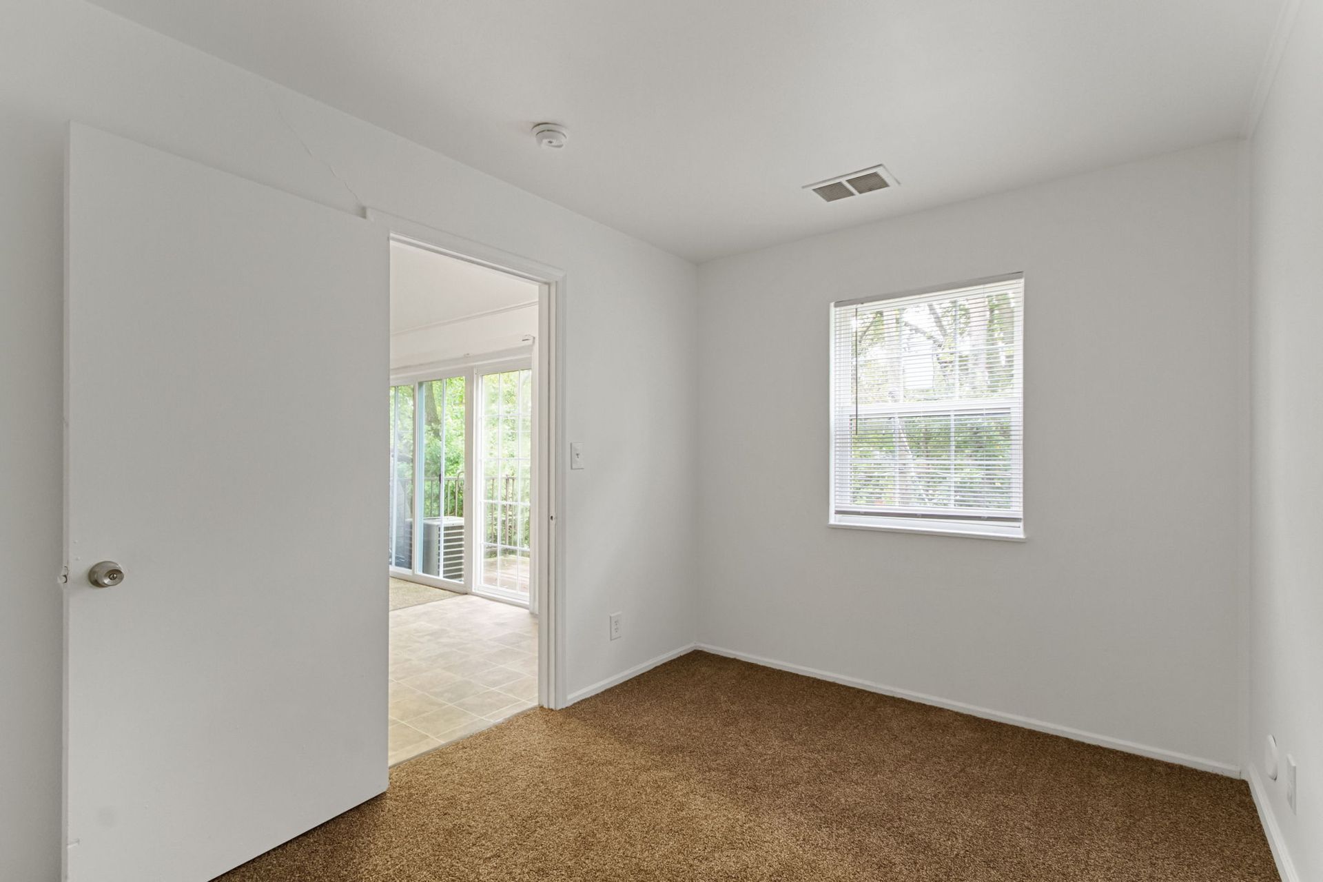 Empty room with brown carpet, white walls, open doorway, and a window with blinds.