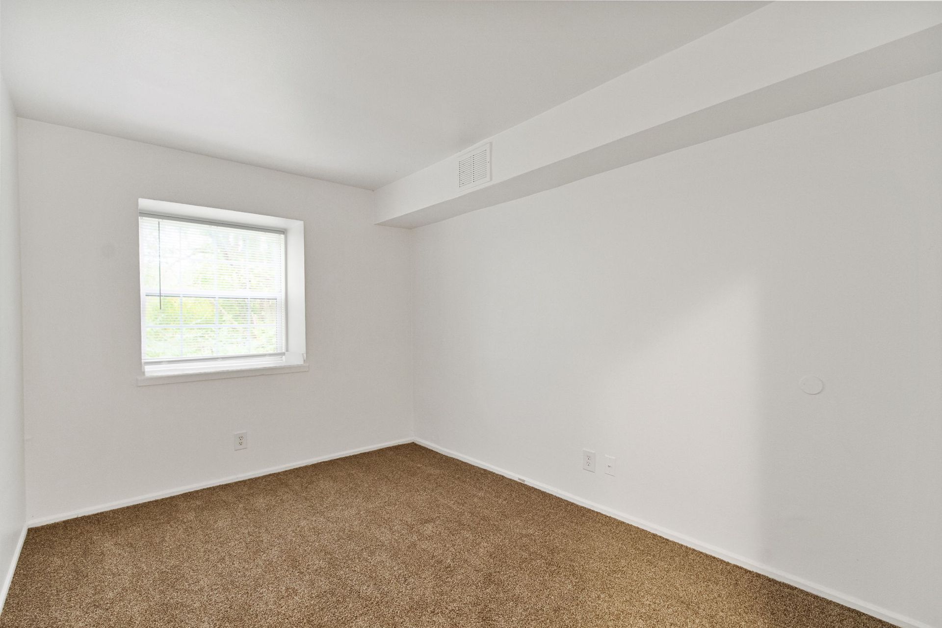 Empty room with brown carpet, white walls, window, and overhead beam.