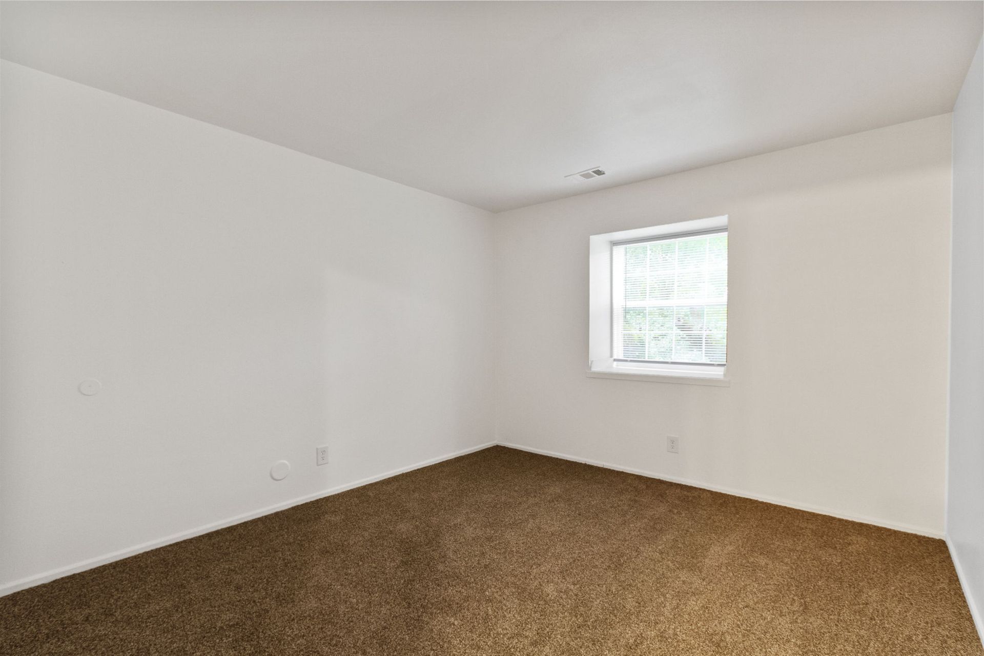 Empty room with brown carpet, white walls, and a window with a blind.
