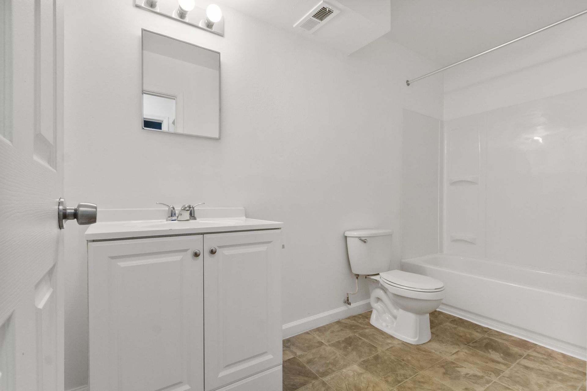 White bathroom with a sink, toilet, and bathtub; white walls and neutral floor.