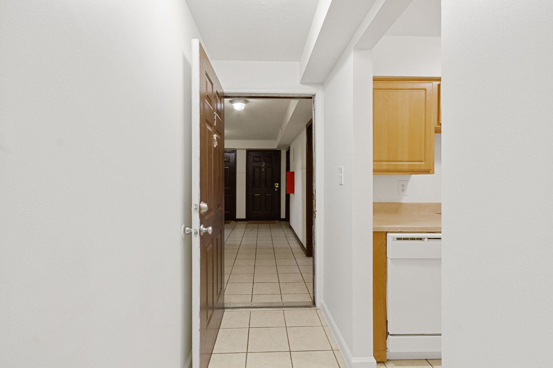 Hallway with open door leading to other doors, kitchen area visible on right.