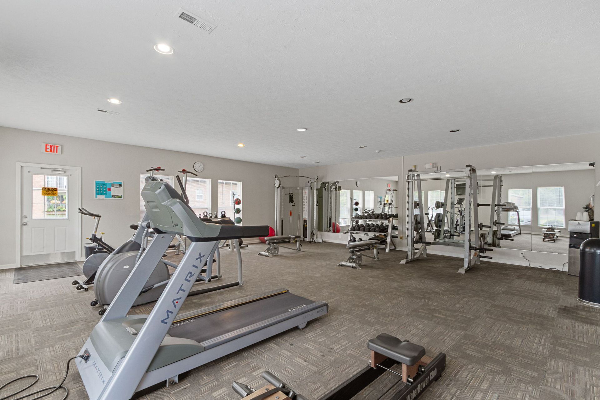Gym with treadmills, stationary bikes, weight machines, mirrors, and exit door.