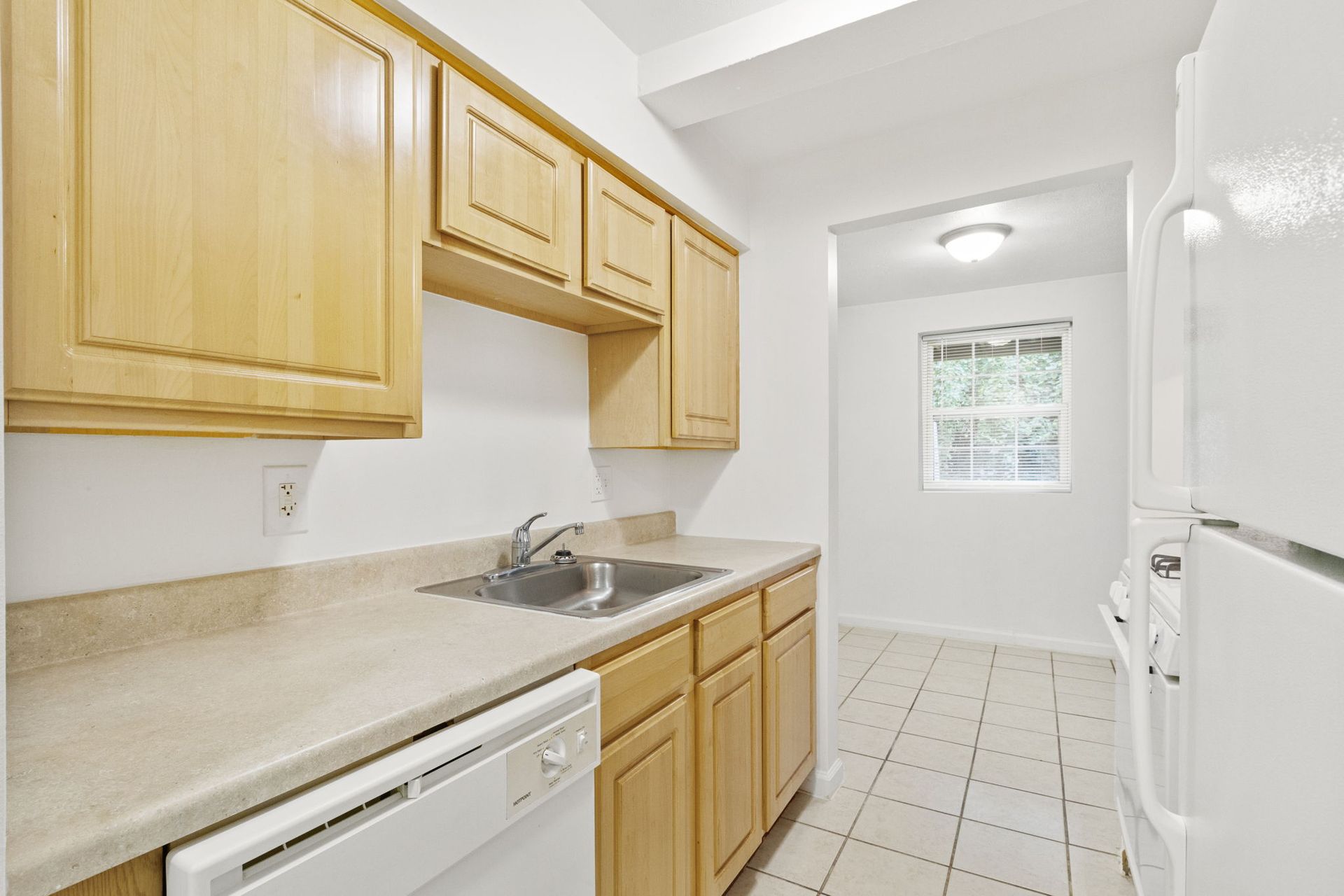 Kitchen with light wood cabinets, white appliances, beige countertop, and tiled floor.