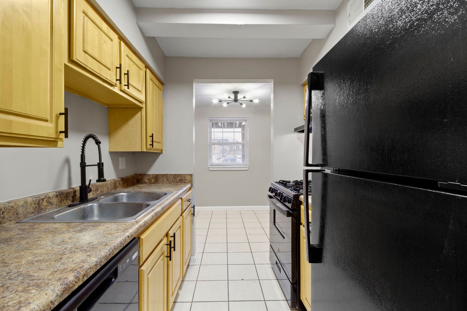 Kitchen with golden cabinets, black appliances, and a window at the far end.