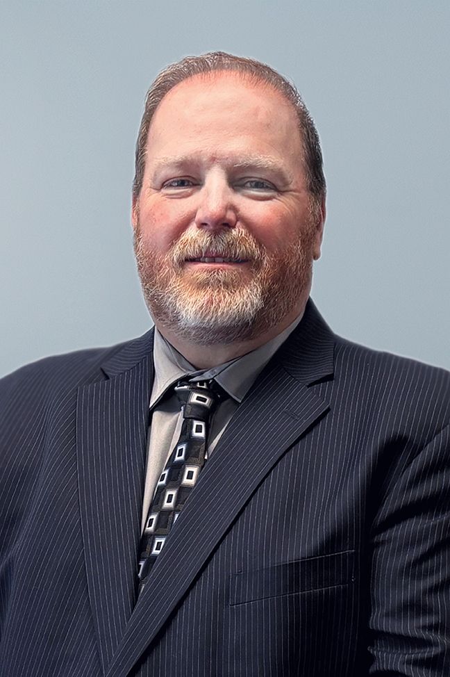 A man in a suit and tie is standing in front of a bush.