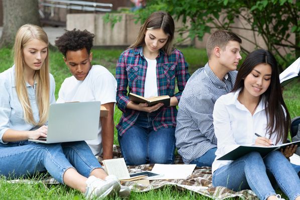 A group of young people are sitting on a blanket in the grass.