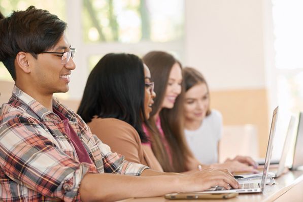 A group of young people are sitting at a table using laptops.