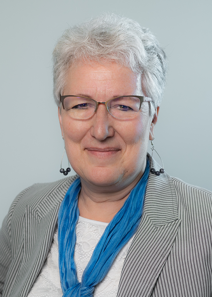 A woman wearing a black jacket and gold hoop earrings smiles for the camera