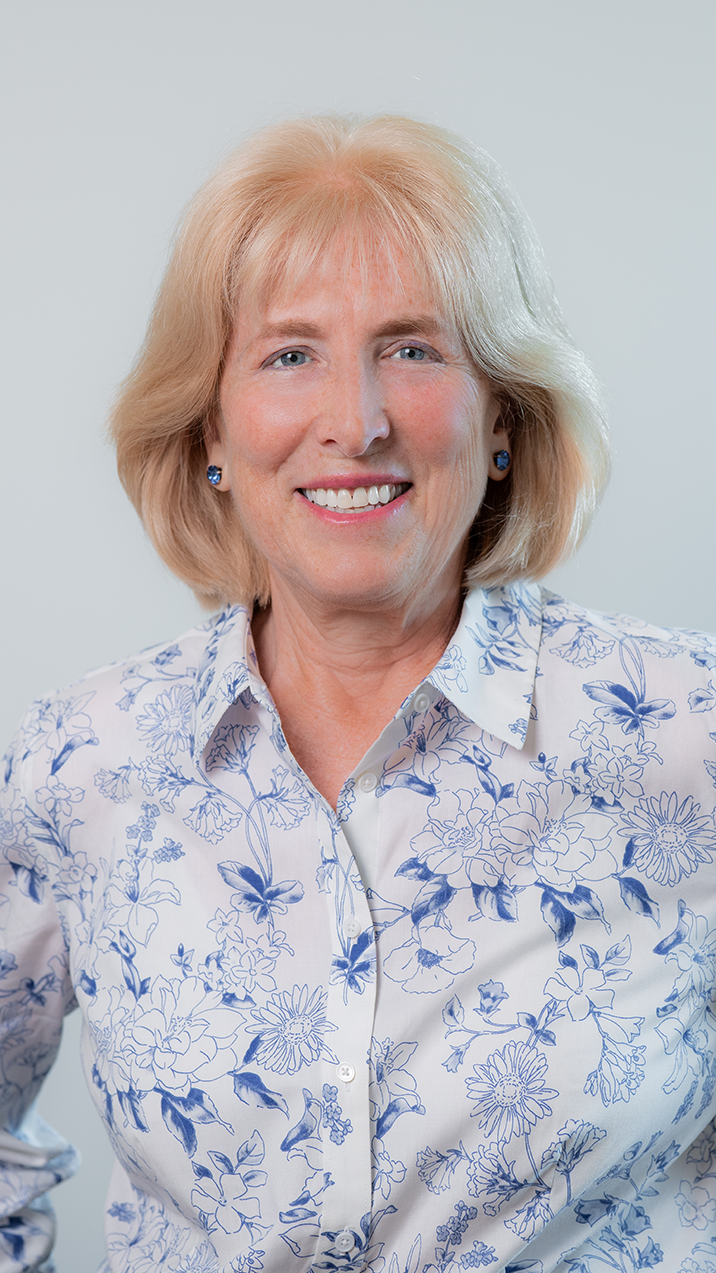 A woman in a blue shirt and black jacket smiles for the camera