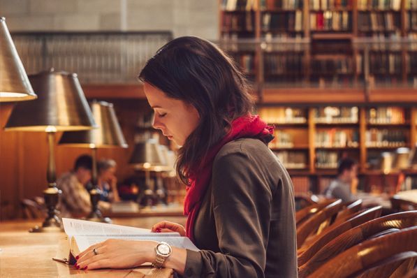 A woman is reading a book in a library.