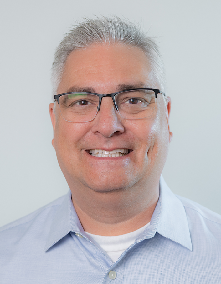 A man in a blue shirt and blue tie is smiling for the camera.