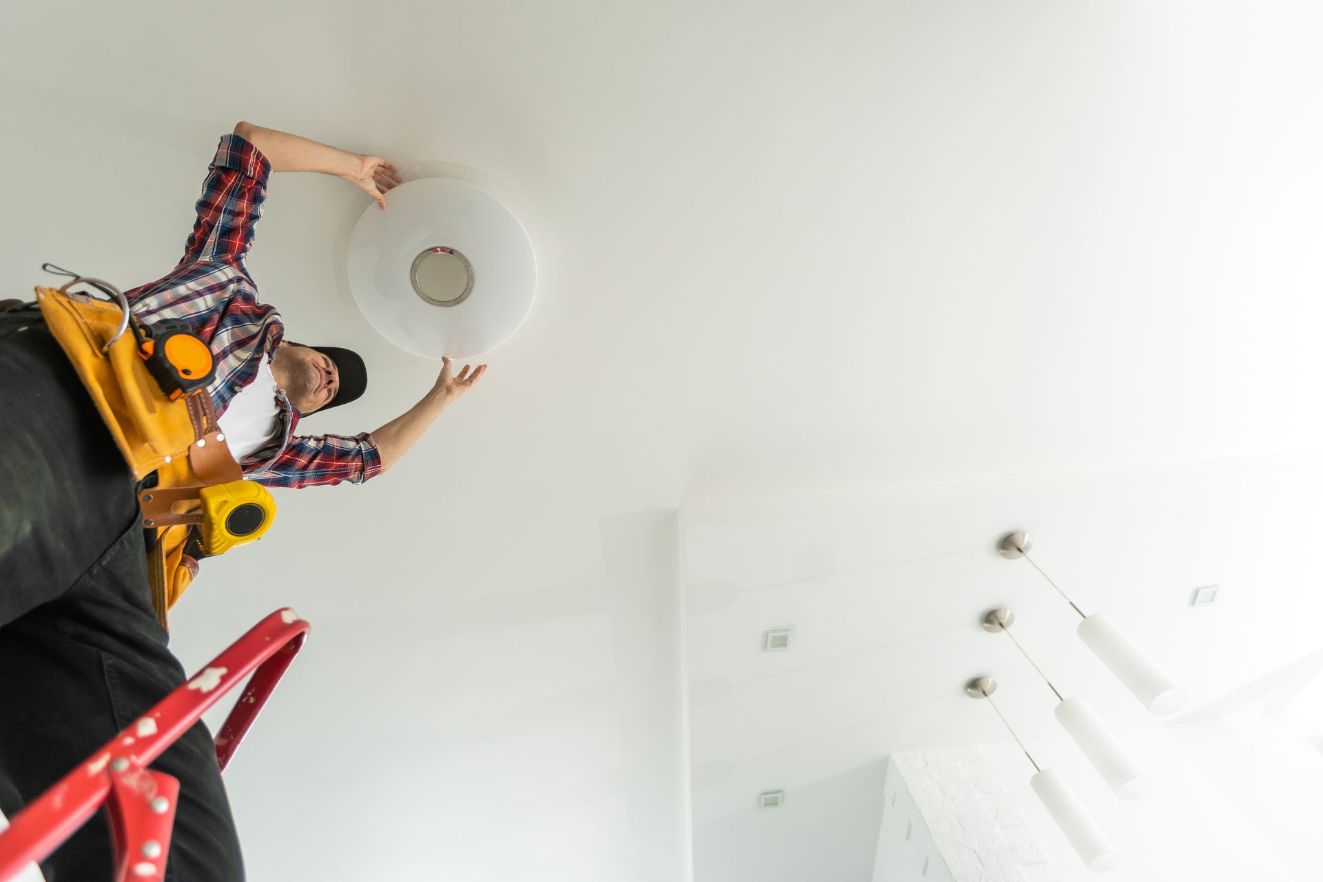 A man is standing on a ladder fixing a light fixture on the ceiling.