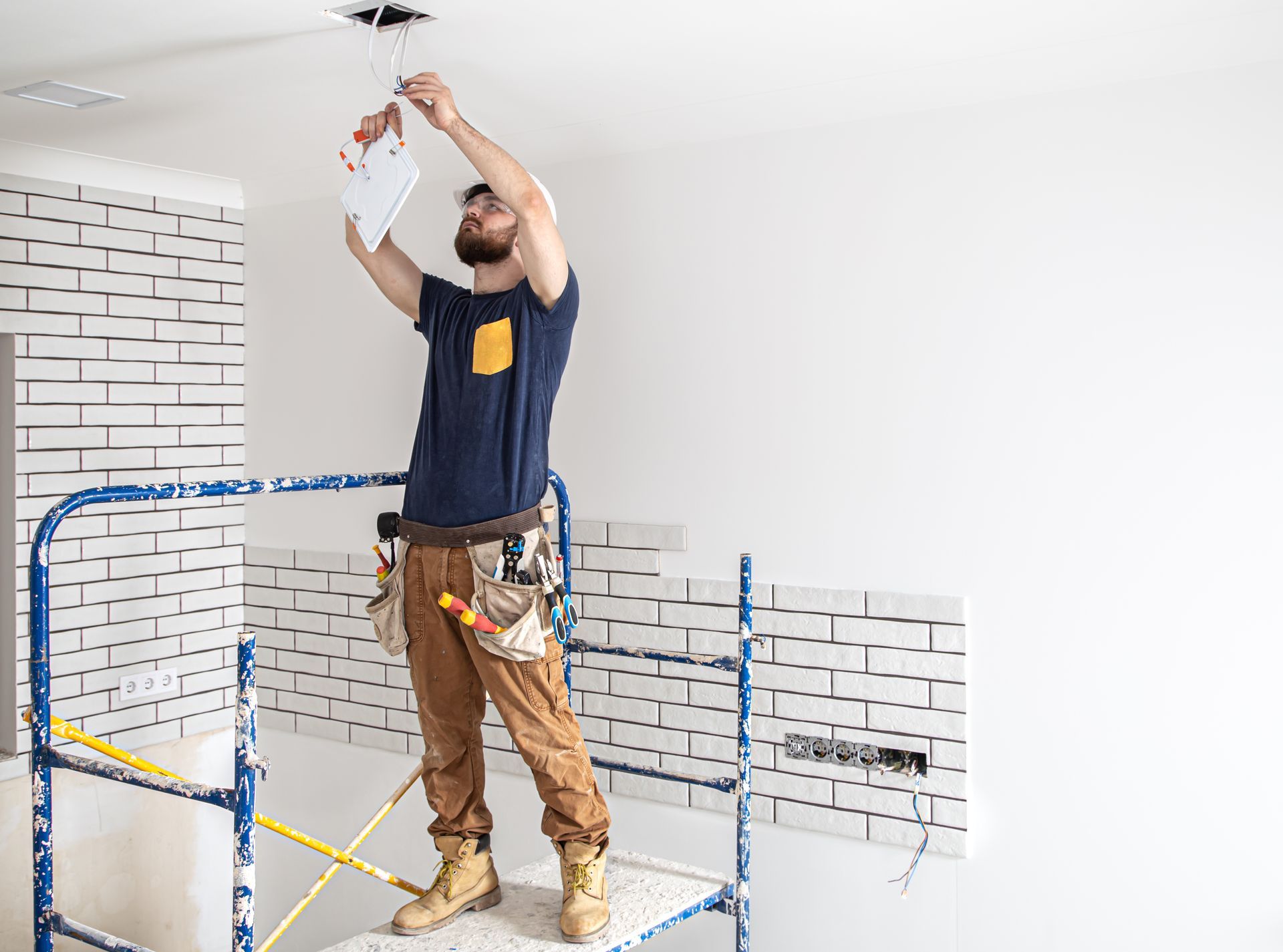 A man is standing on a ladder working on a light fixture.