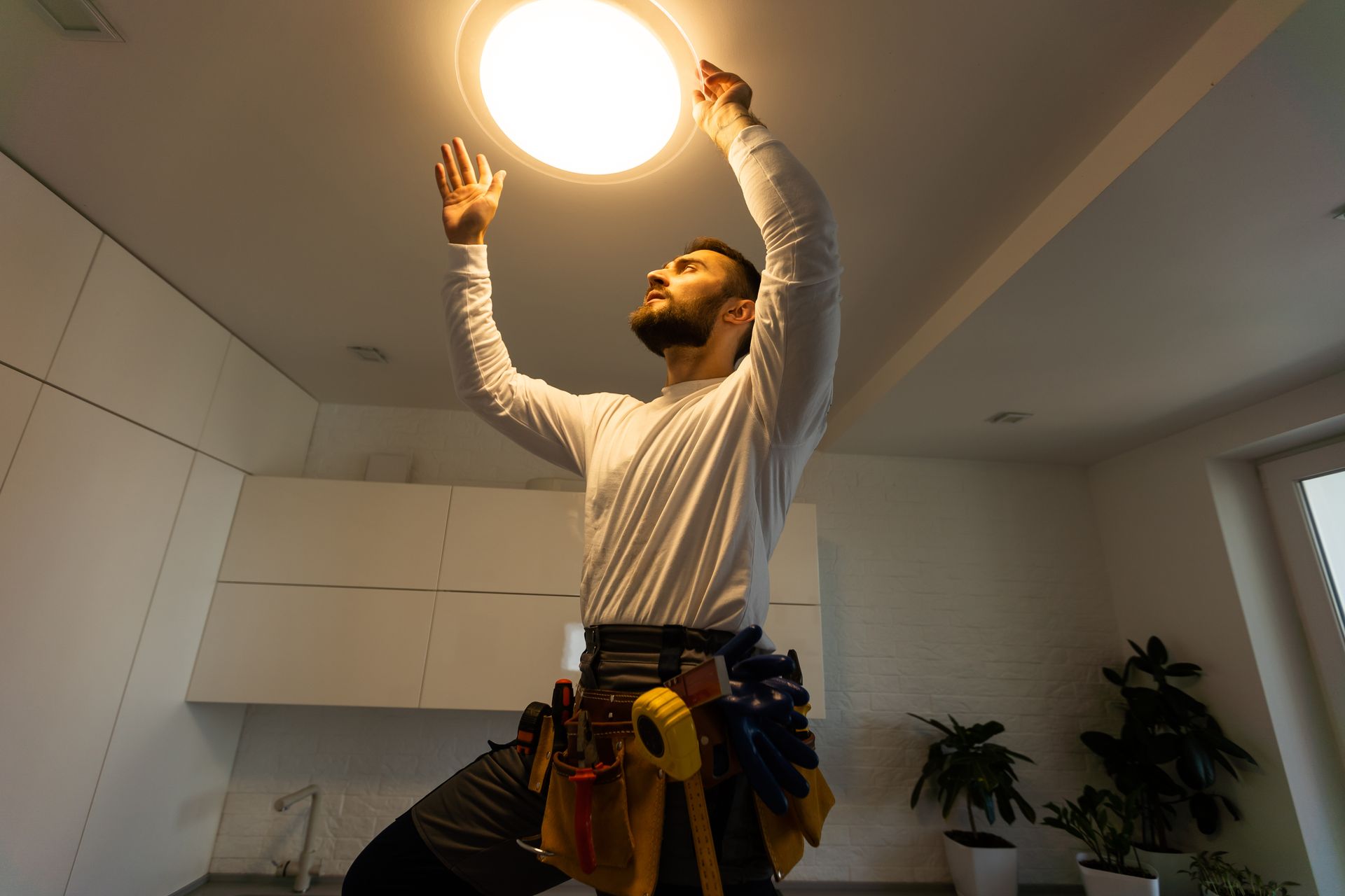 A man is changing a light bulb in a kitchen.