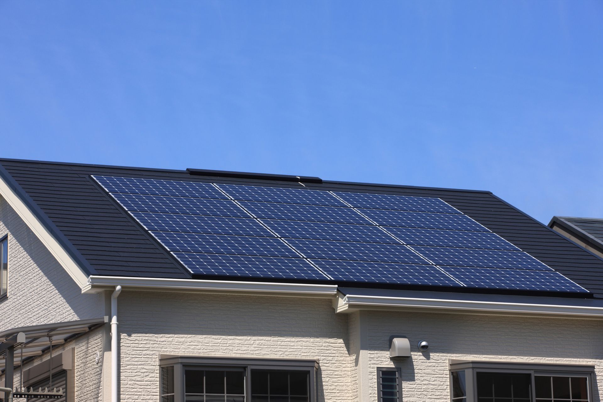 Solar panels installed on the grey tiled roof of a brick house under a clear blue sky.