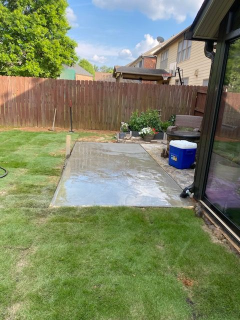 A backyard with a lawn , a patio , a fence and a blue cooler.