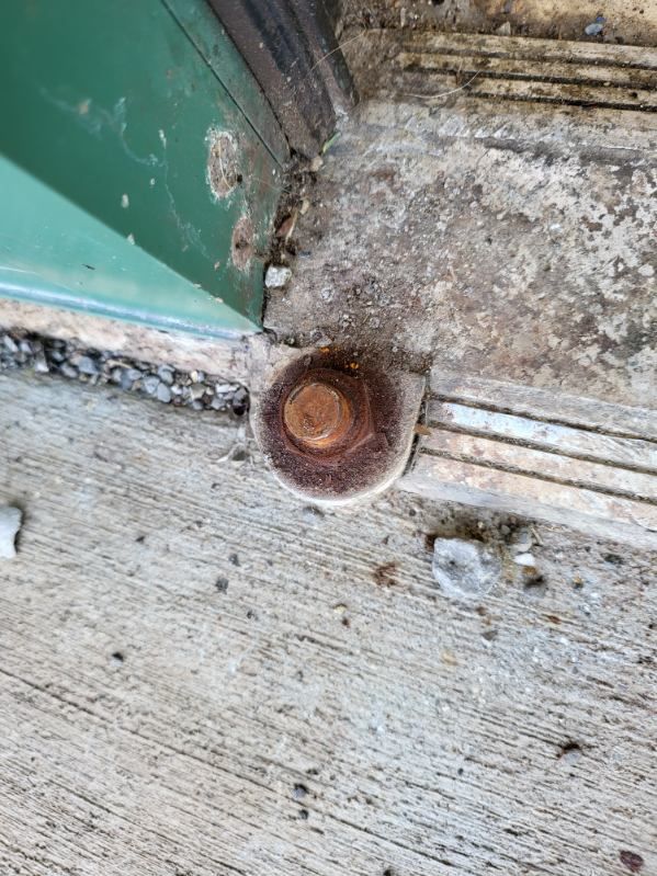 A close up of a rusty bolt on the ground next to a door.
