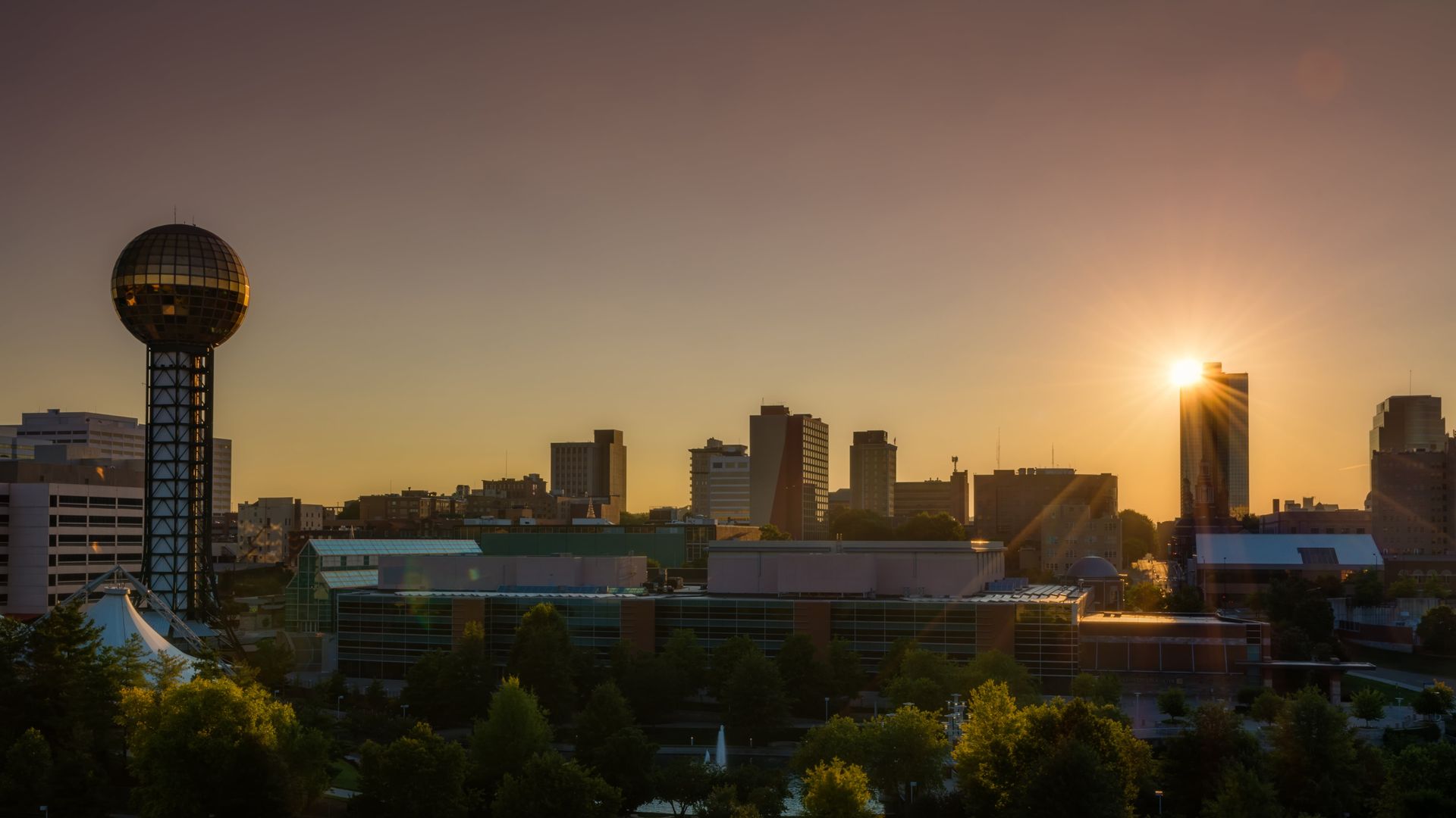 The sun is setting over a city with a clock tower in the foreground.