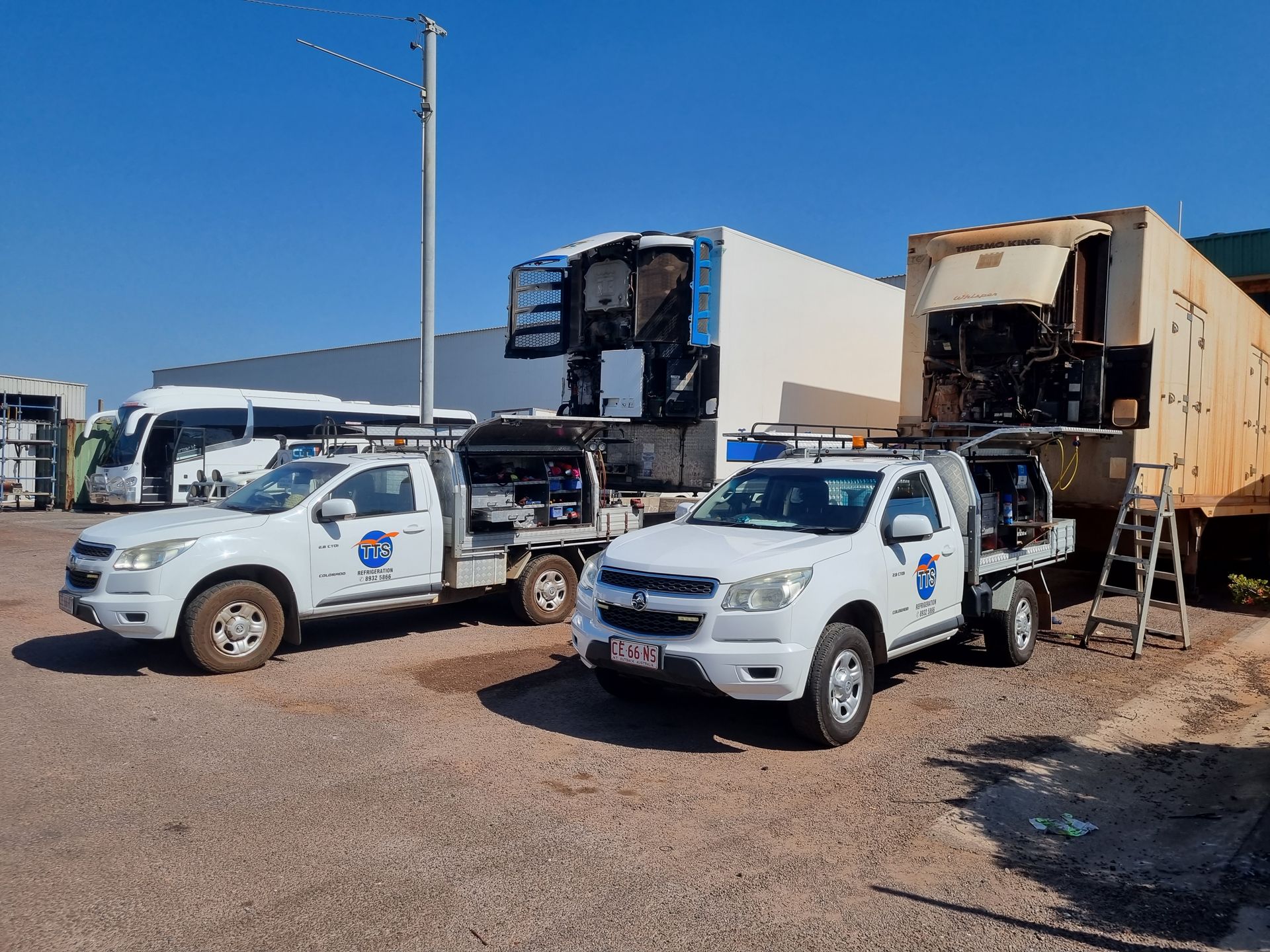 Two white trucks parked near bus and trailer in an outdoor lot under a blue sky — TTS Refrigeration in Pinelands, NT