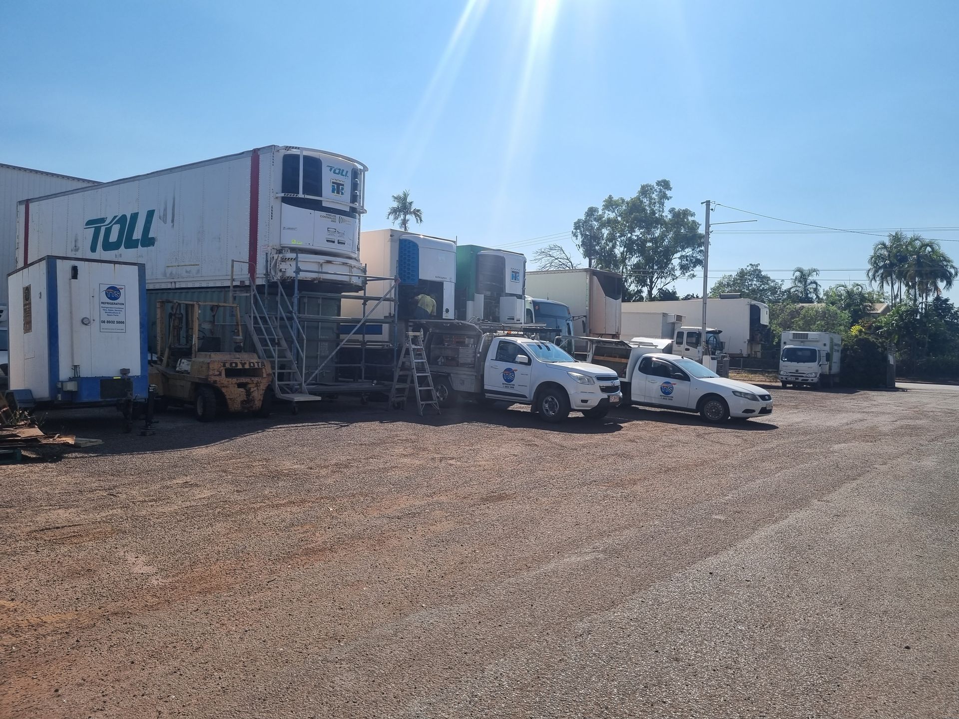 White refrigerated trucks and vehicles with blue and white logos parked outside a building on a gravel lot — TTS Refrigeration in Pinelands, NT