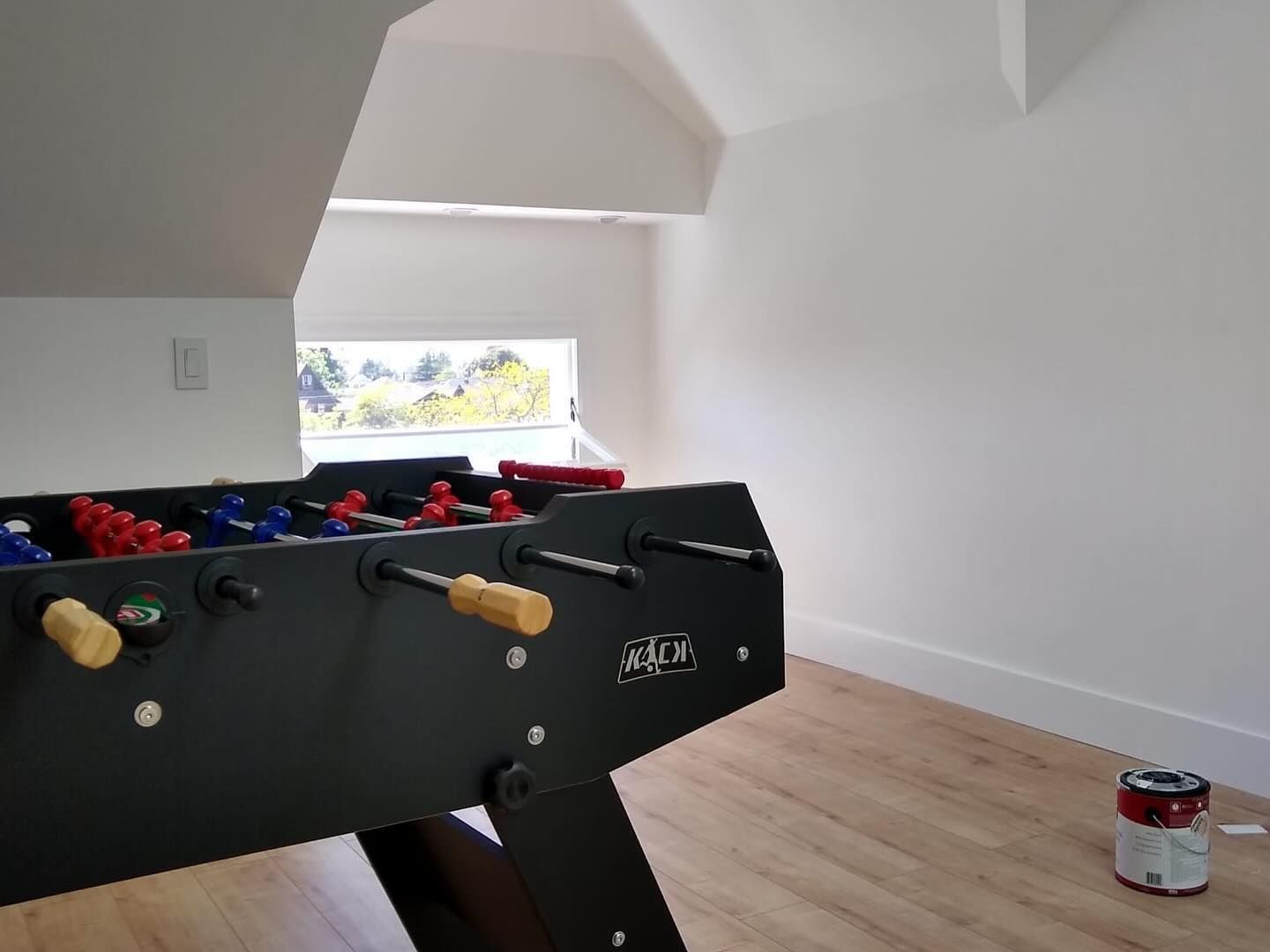 A foosball table is sitting in a room next to a window.