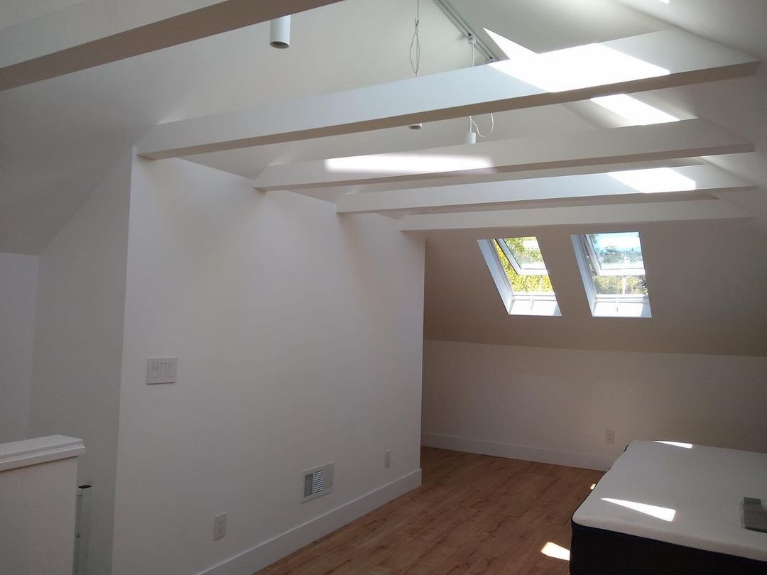 A room with white walls and wooden floors and a skylight in the ceiling.