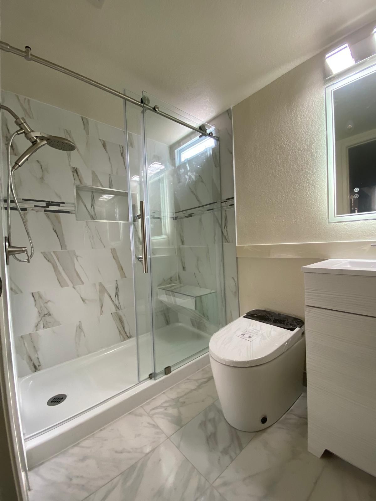 A bathroom with a toilet , sink , shower and mirror.