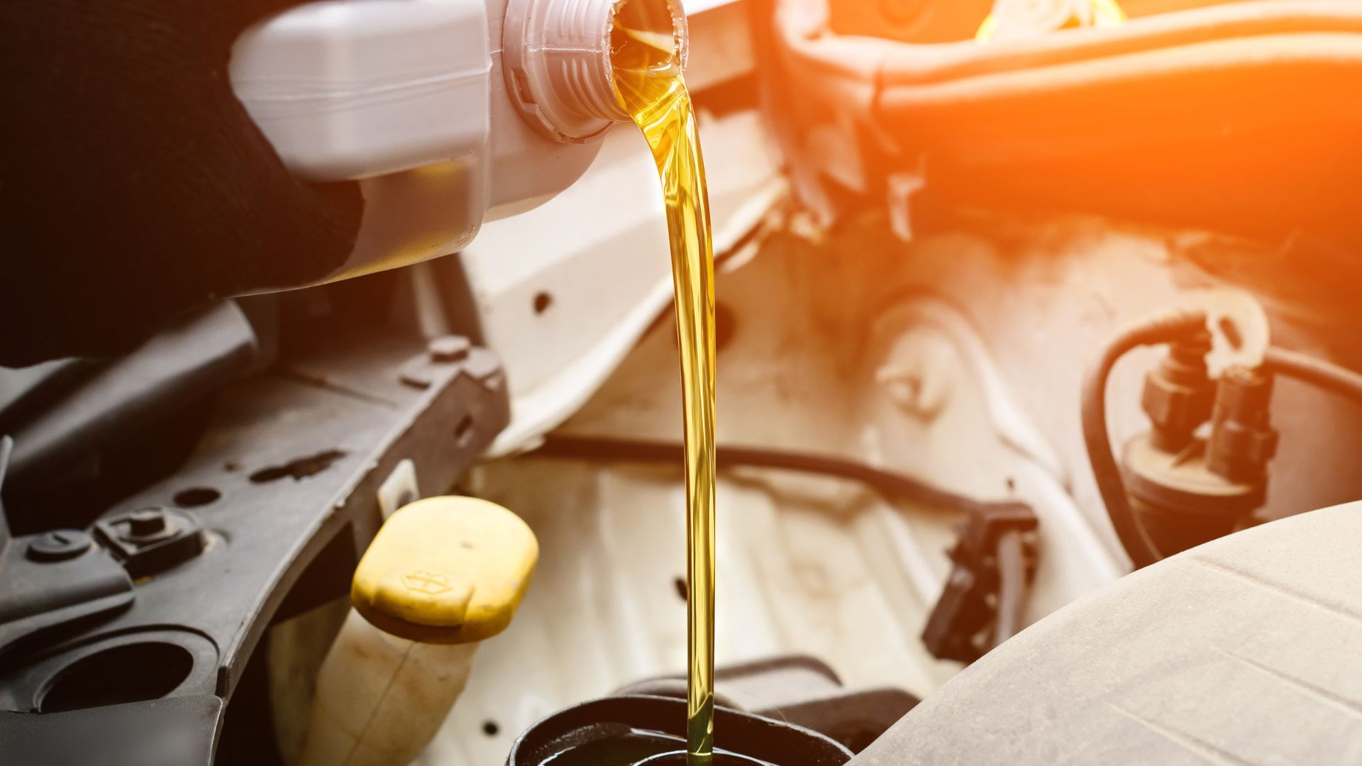 A close up of a person pouring oil into a car.