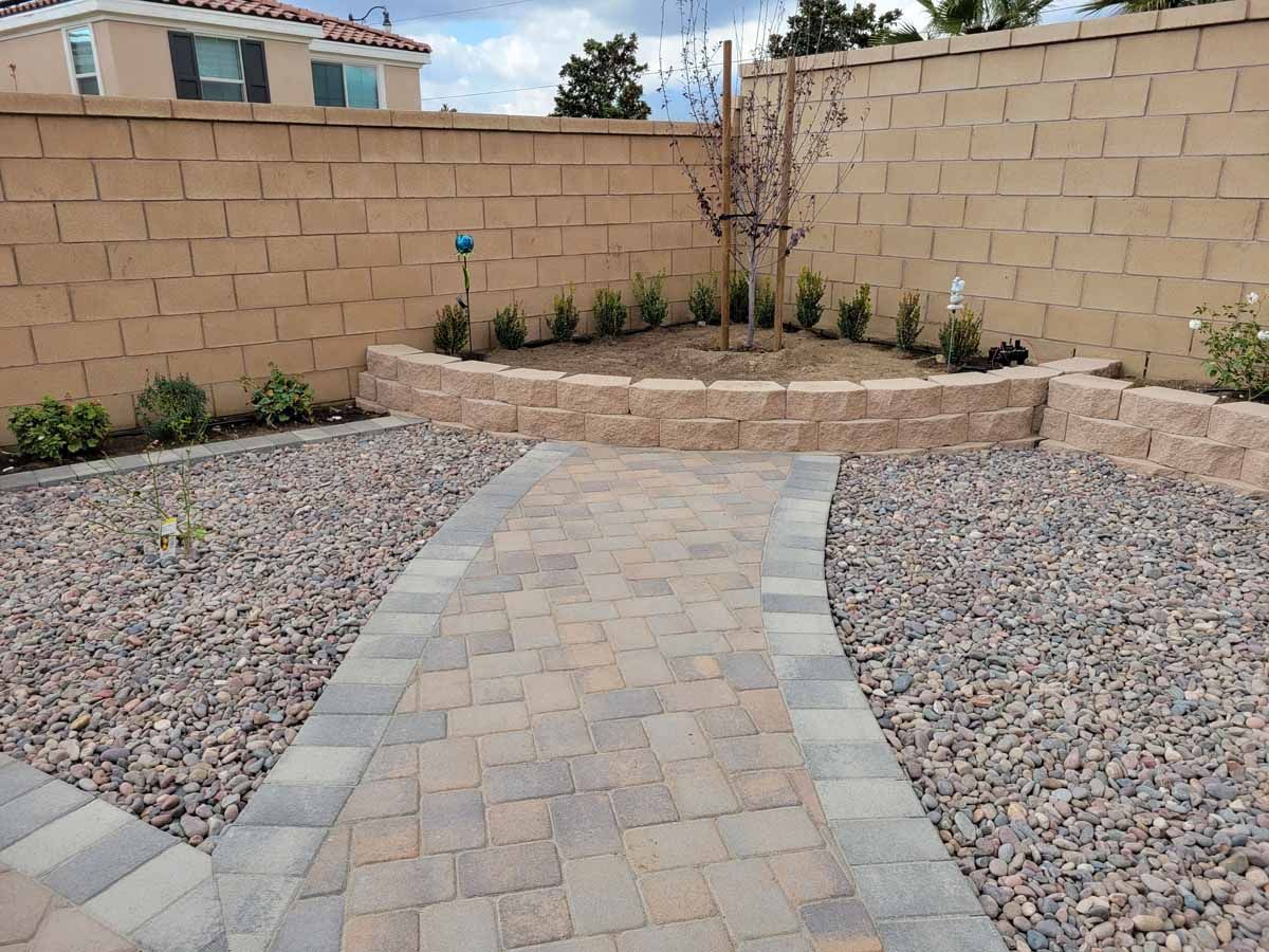 A brick walkway leading to a stone wall in a backyard.
