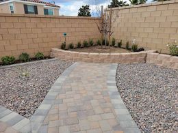 A brick walkway leading to a stone wall in a backyard.