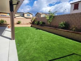 A backyard with a lush green lawn and a brick wall.