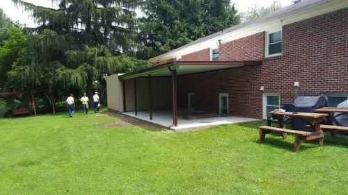 A group of people standing in front of a brick building with a picnic table and grill.
