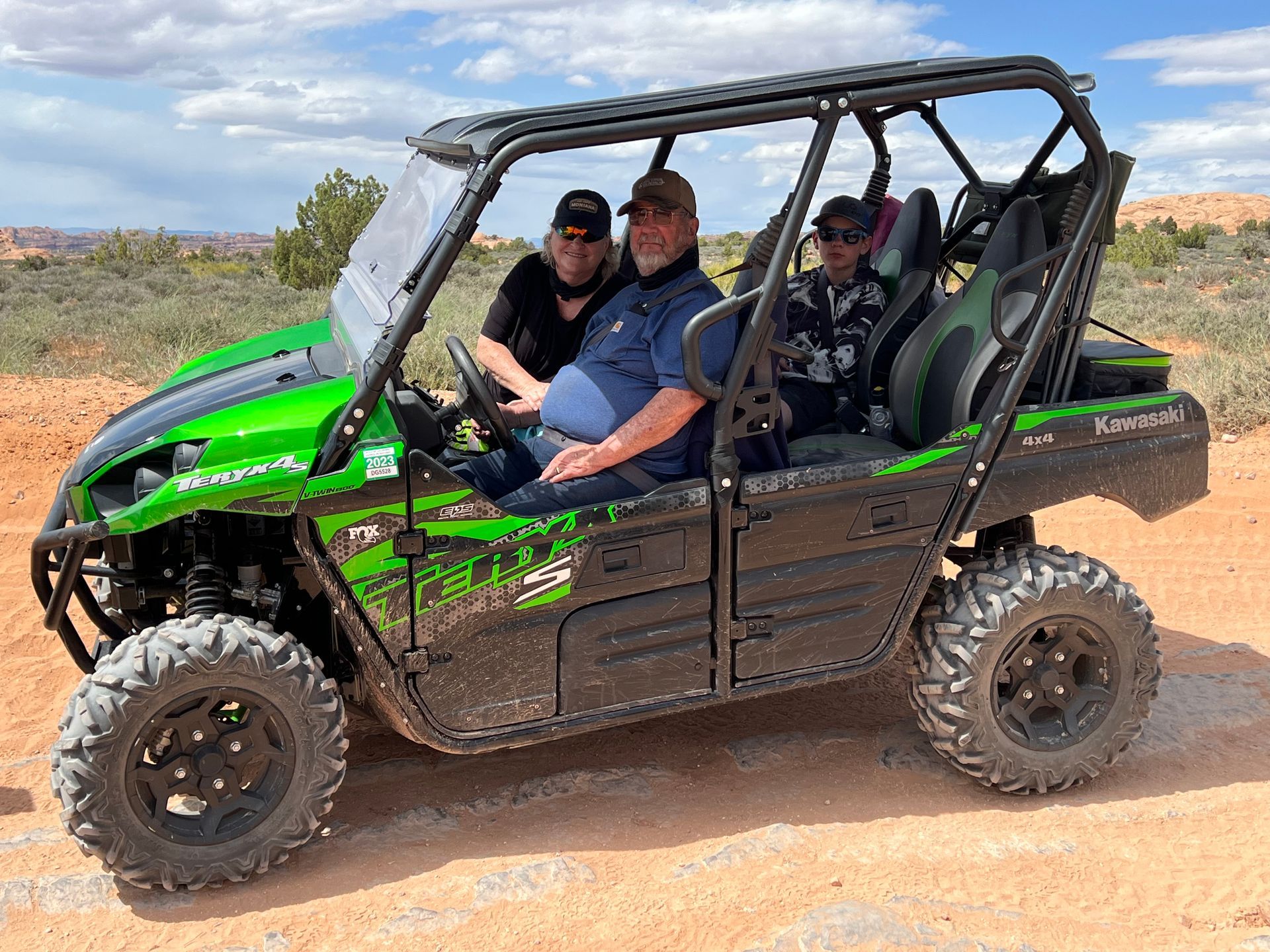 A group of people are sitting in a green atv on a dirt road.