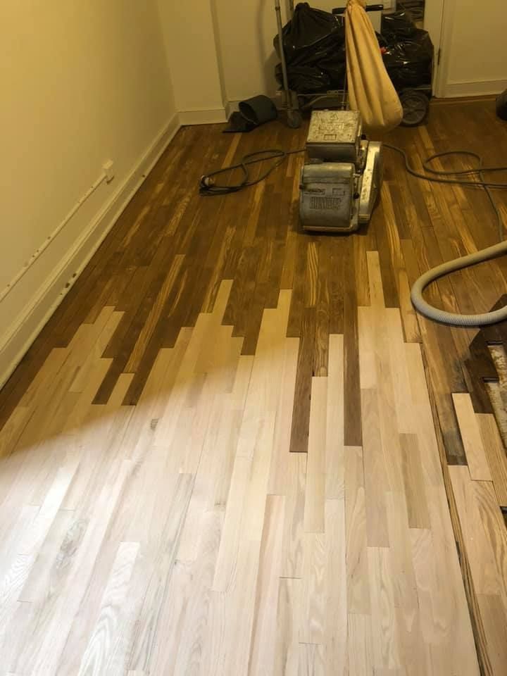 Wood floor sanding, half complete. Lighter wood contrasts darker, refinished area. Sanding machine visible.