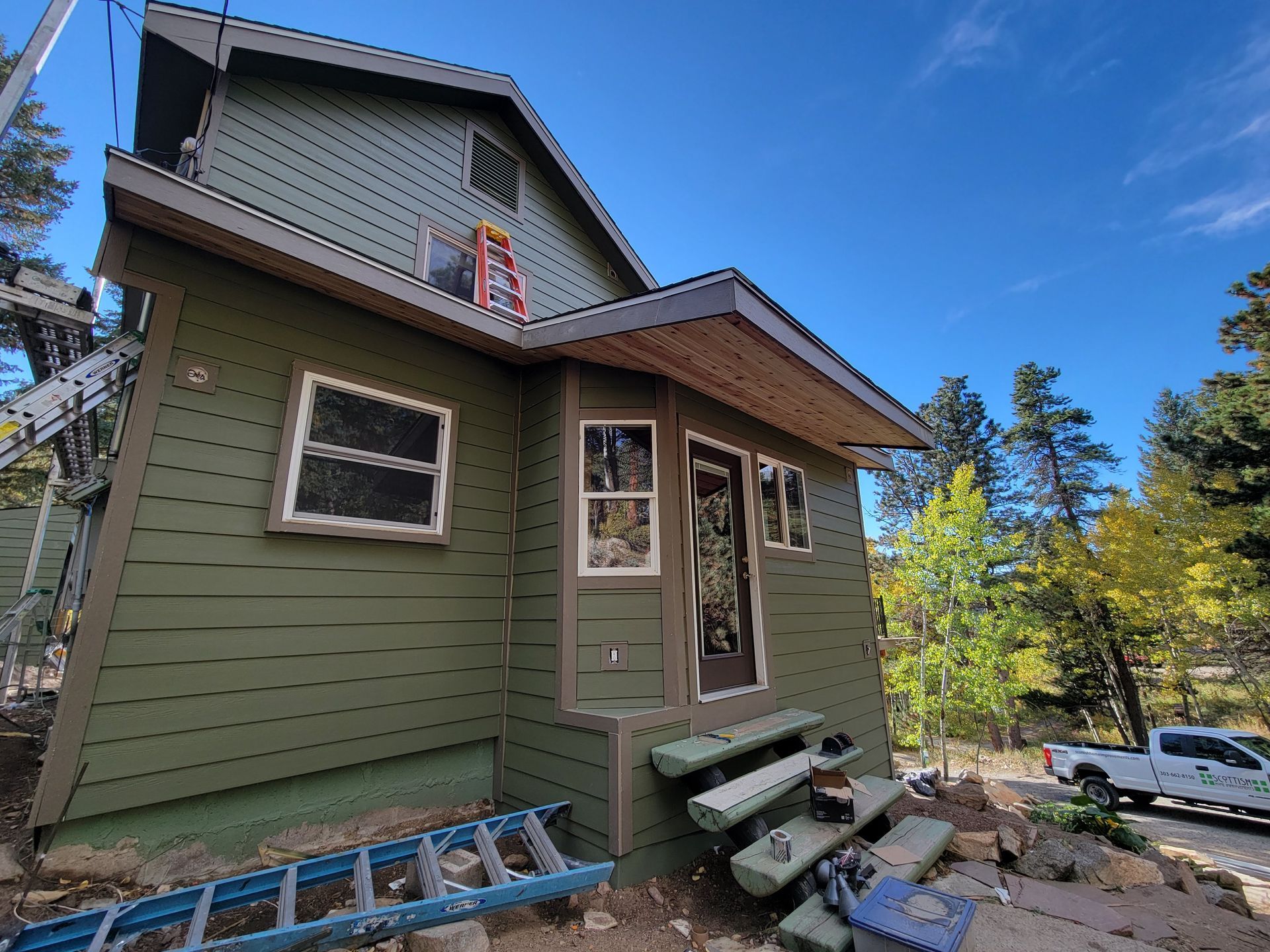 A green house with a ladder in front of it is being painted.