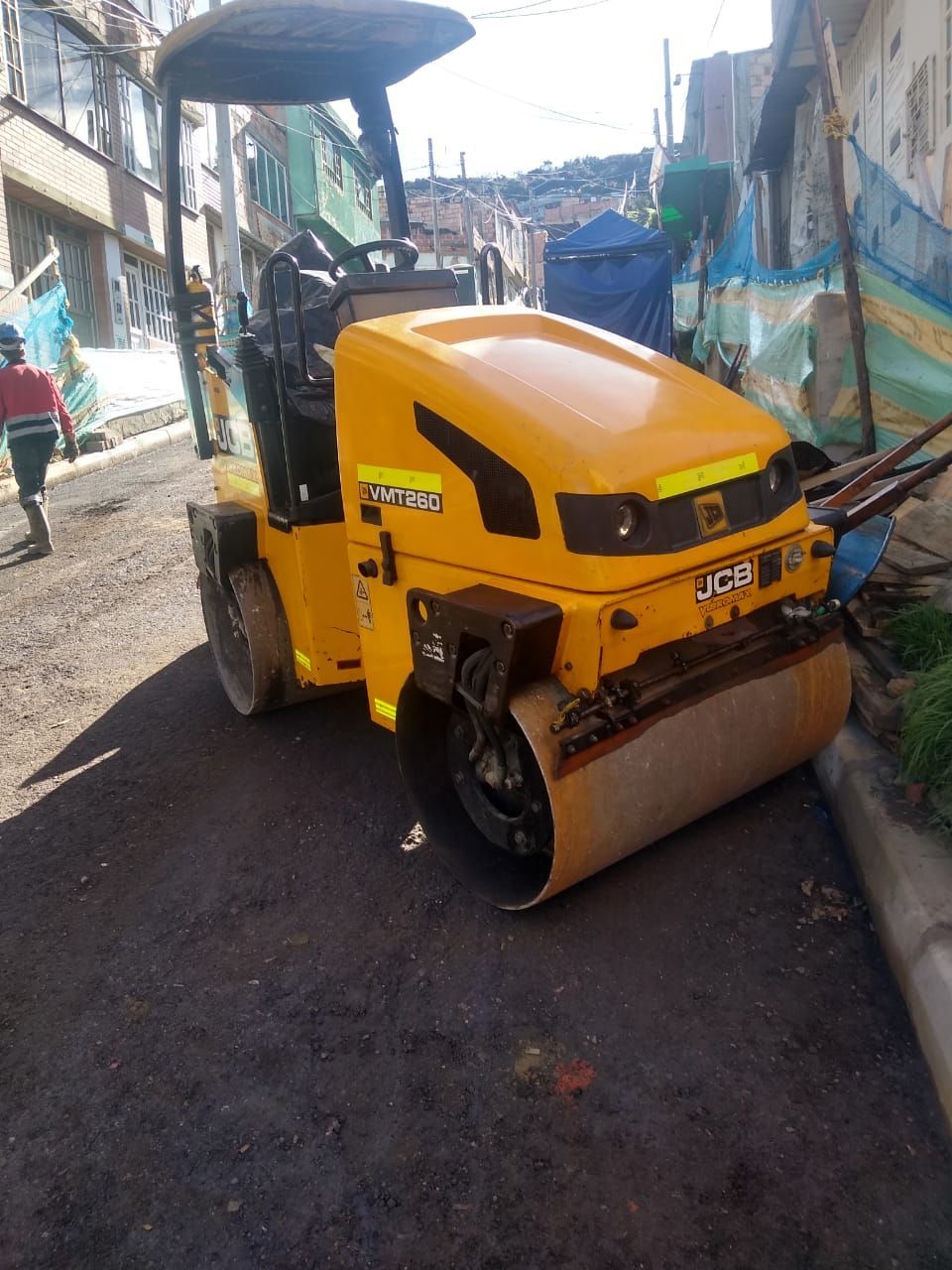 Una apisonadora amarilla estacionada en una calle estrecha con edificios a ambos lados.