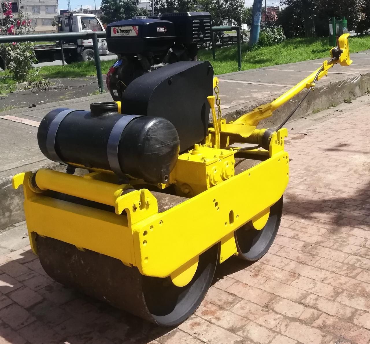 Apisonadora amarilla con tanque negro estacionada en un camino de ladrillos al aire libre.