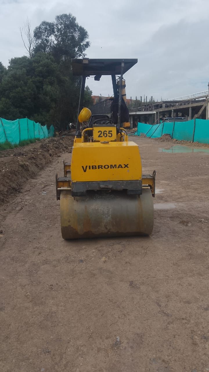 Apisonadora amarilla estacionada en una obra de construcción de tierra, vista frontal.