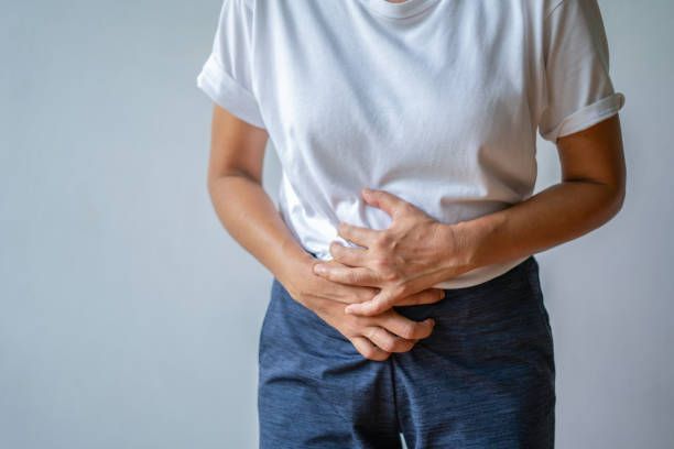 A person in a white shirt and blue pants clutches their stomach, indicating abdominal pain.