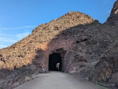 Mobile IVTherapyLas Vegas-A rugged mountain landscape with a dirt path leading into a dark tunnel carved into the rock. The sky is clear, creating a serene and adventurous tone.