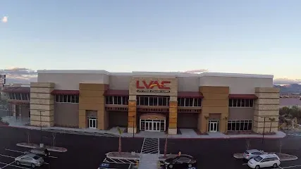 Mobile IV Therapy Las Vegas-Front view of a large fitness center with LVAC signage, beige and brown exterior, modern design elements, and cars parked out front under a clear sky.
