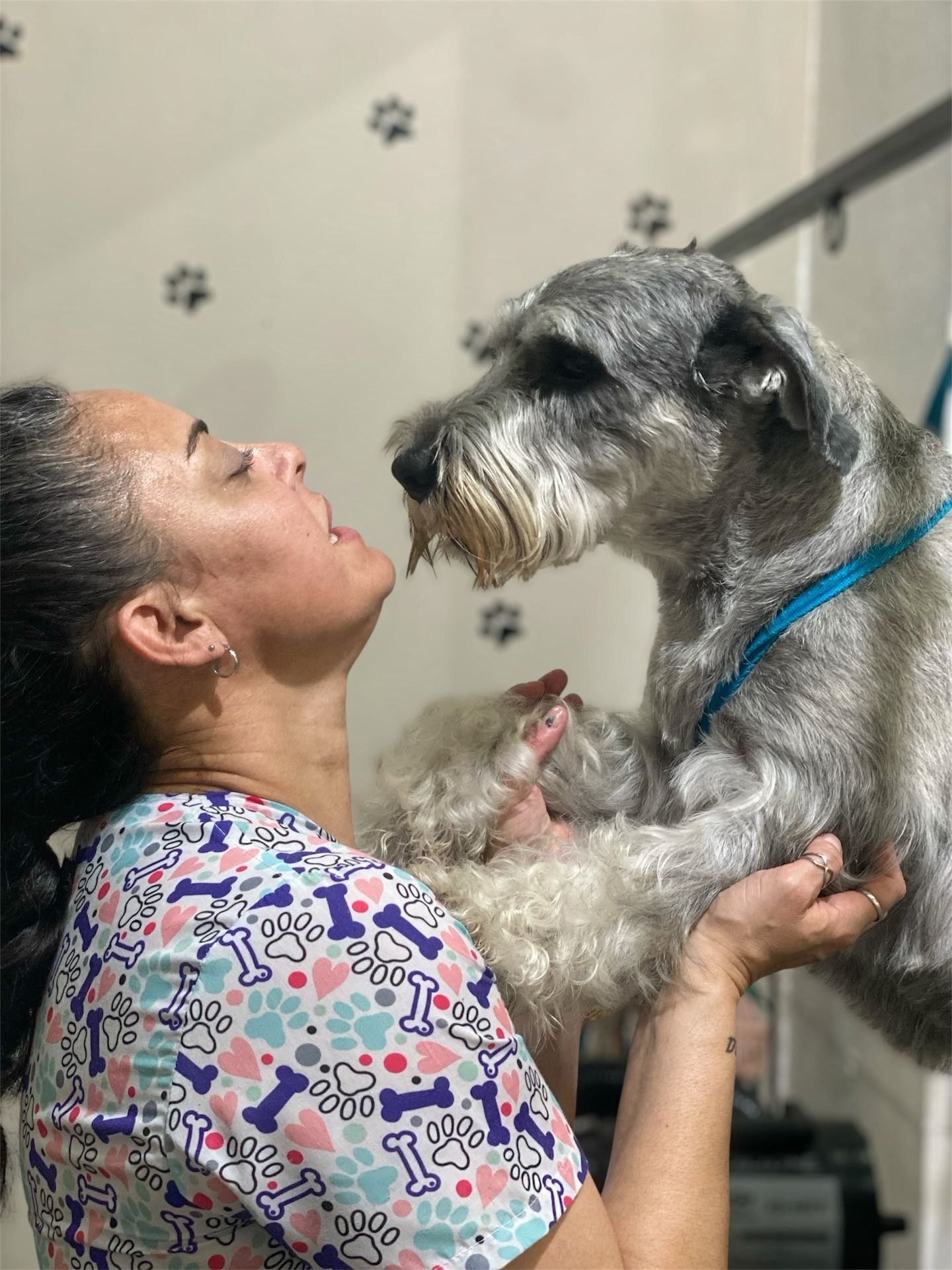 Mujer sosteniendo un perro negro, con sombrero y suéter blanco, al aire libre.